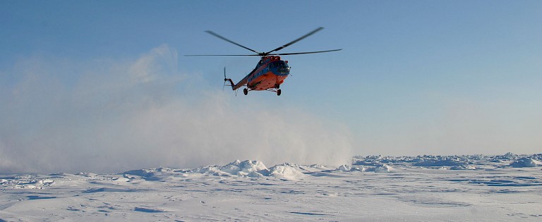 De landende helikopter doet veel sneeuw opwaaien.