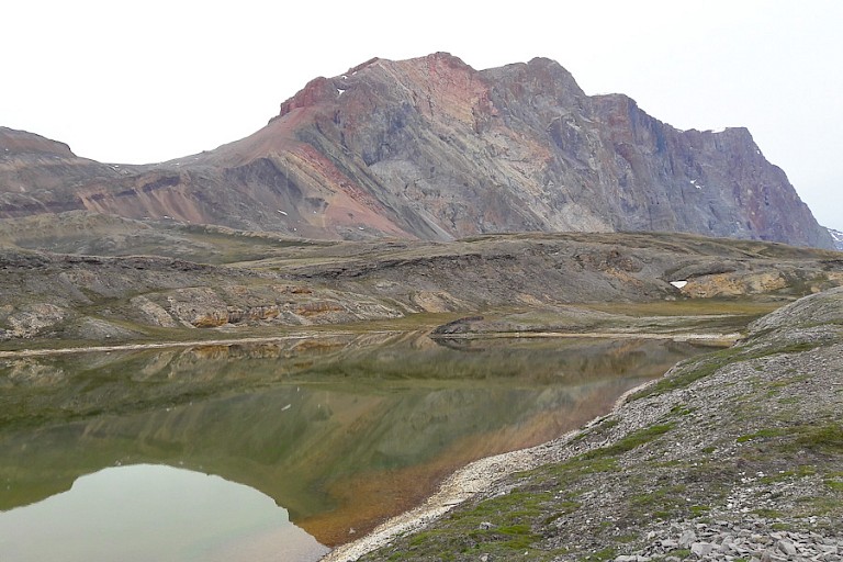 Tijdens een wandeling over Ella Island komen we uit bij een meer en hebben we uitzicht op de prachtige gekleurde rotspartij, Kong Oscar Fjord.